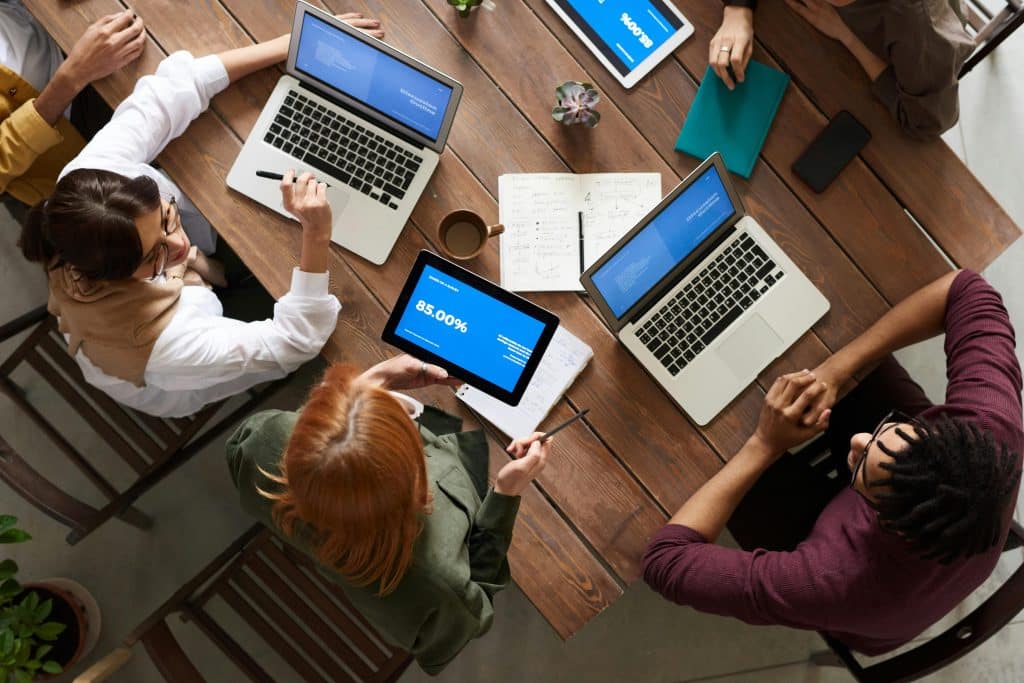 a top down image of people sitting around a table while using their devices and chatting.